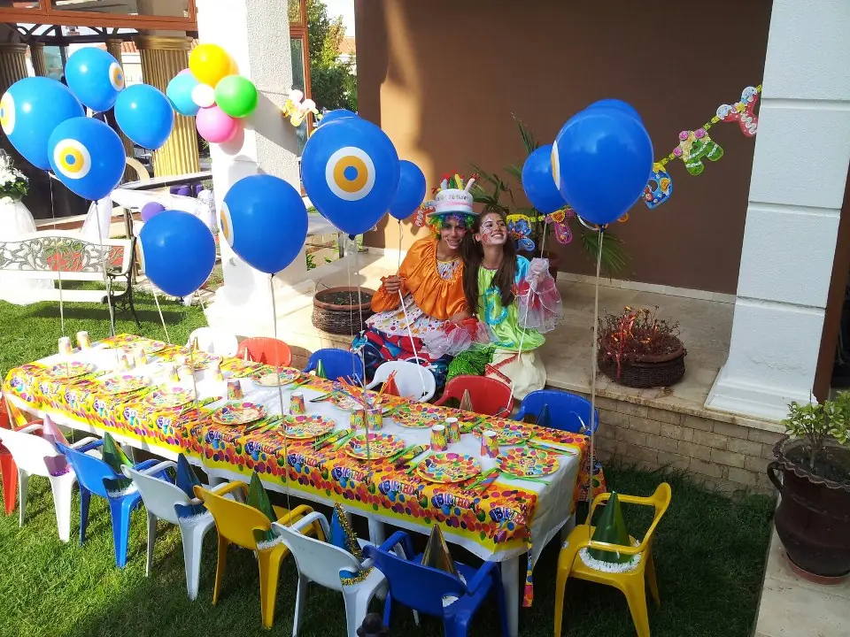 Bahçede kurulmuş doğum günü masası, mavi balonlar ve palyaço